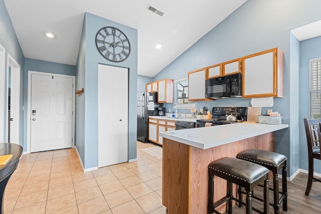 kitchen with kitchen peninsula, vaulted ceiling, a kitchen bar, light tile patterned floors, and black appliances