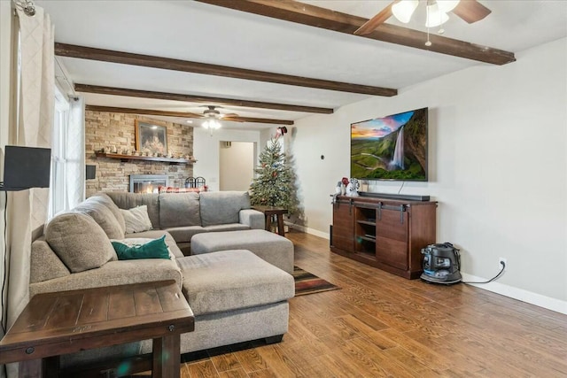 living room with beamed ceiling, ceiling fan, a stone fireplace, and wood-type flooring