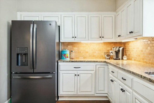 kitchen with backsplash, light stone countertops, white cabinets, and stainless steel refrigerator with ice dispenser