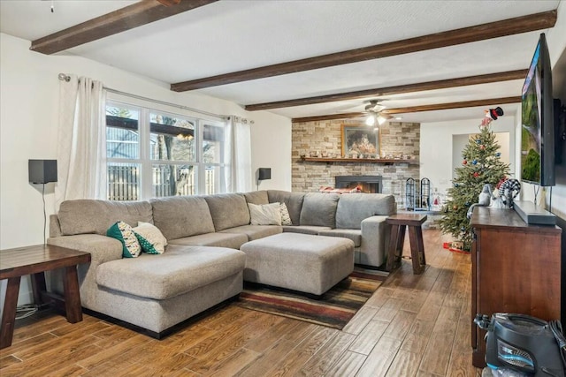 living room featuring ceiling fan, a fireplace, and beamed ceiling