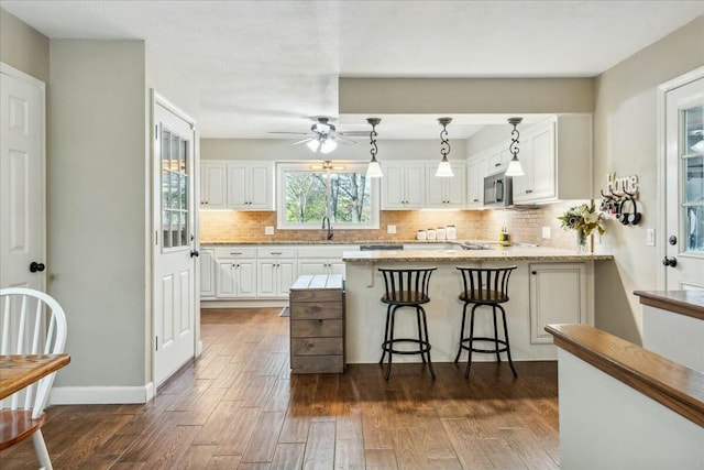 kitchen with hanging light fixtures, white cabinetry, dark hardwood / wood-style flooring, and light stone countertops