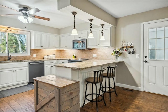 kitchen with sink, hardwood / wood-style flooring, appliances with stainless steel finishes, decorative light fixtures, and white cabinetry