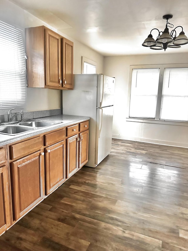 kitchen featuring dark wood-type flooring, sink, pendant lighting, an inviting chandelier, and white fridge