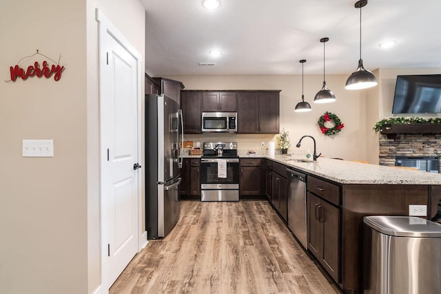 kitchen with sink, hanging light fixtures, appliances with stainless steel finishes, dark brown cabinets, and kitchen peninsula