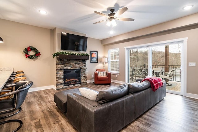 living room with hardwood / wood-style flooring, ceiling fan, and a stone fireplace