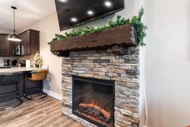 interior space with pendant lighting, a stone fireplace, light hardwood / wood-style floors, light stone counters, and dark brown cabinetry