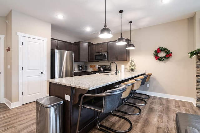 kitchen featuring kitchen peninsula, appliances with stainless steel finishes, dark brown cabinets, sink, and decorative light fixtures