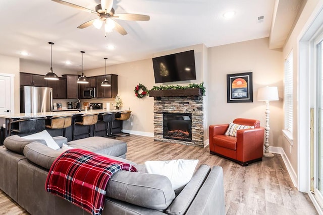 living room featuring a fireplace, light wood-type flooring, ceiling fan, and sink