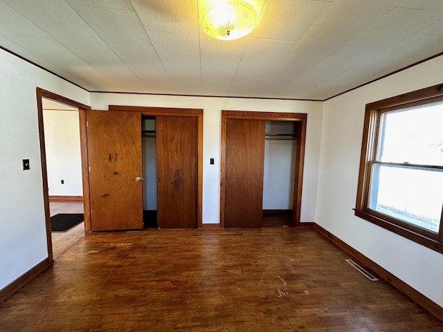 unfurnished bedroom featuring dark hardwood / wood-style floors and multiple closets