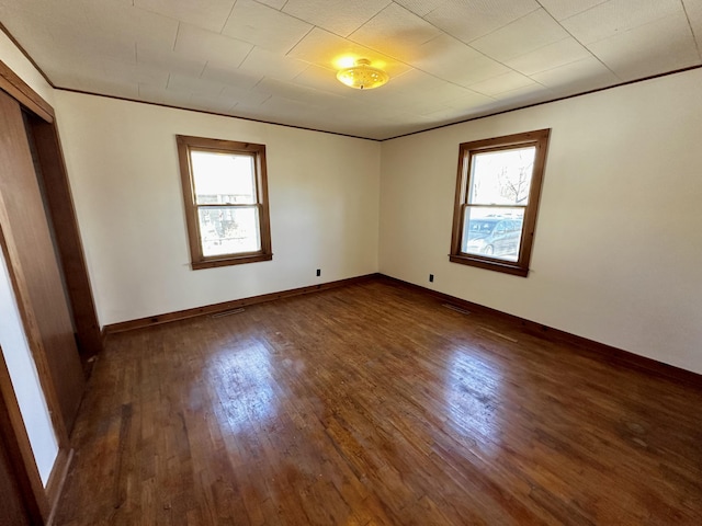 empty room with crown molding, dark wood-type flooring, and a healthy amount of sunlight