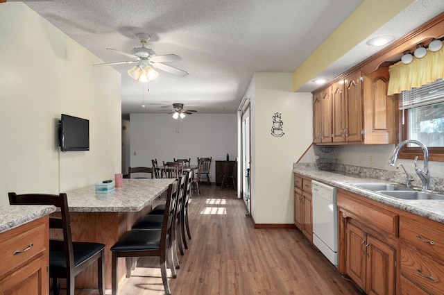 kitchen with dishwasher, sink, wood-type flooring, a textured ceiling, and a kitchen bar