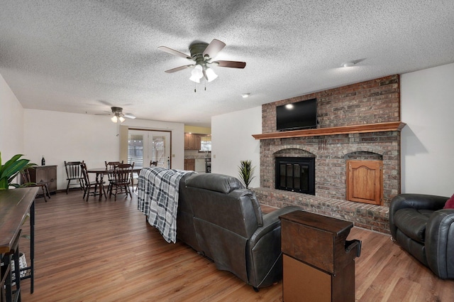 living room with ceiling fan, a fireplace, light hardwood / wood-style floors, and a textured ceiling