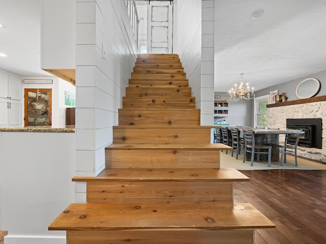 stairway featuring a fireplace, hardwood / wood-style flooring, and an inviting chandelier