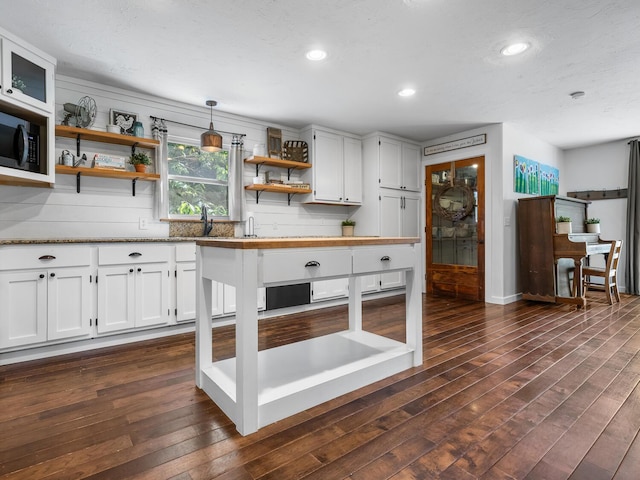 kitchen with white cabinetry, light stone counters, dark hardwood / wood-style floors, pendant lighting, and decorative backsplash