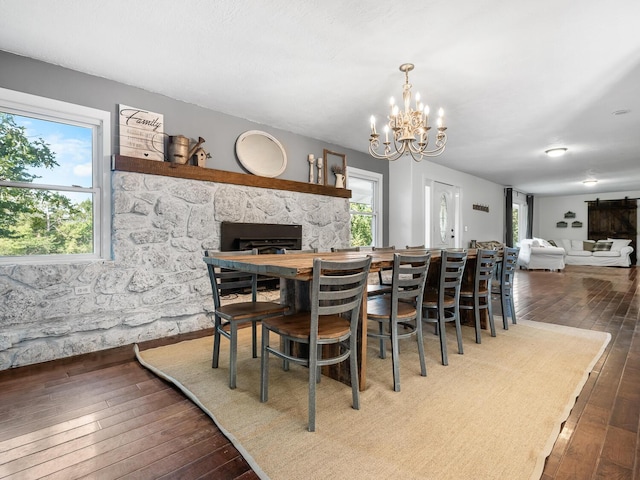 dining space featuring dark hardwood / wood-style flooring, a stone fireplace, and a chandelier