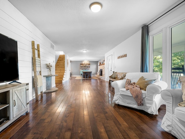 living room featuring a textured ceiling, dark hardwood / wood-style flooring, a stone fireplace, and wooden walls