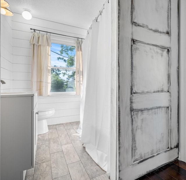 bathroom featuring vanity, a textured ceiling, toilet, and wood walls