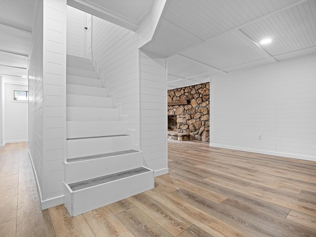 stairs featuring wood-type flooring and a stone fireplace