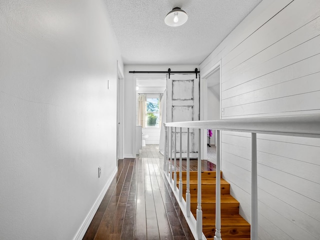 hallway featuring a barn door, wooden walls, dark wood-type flooring, and a textured ceiling