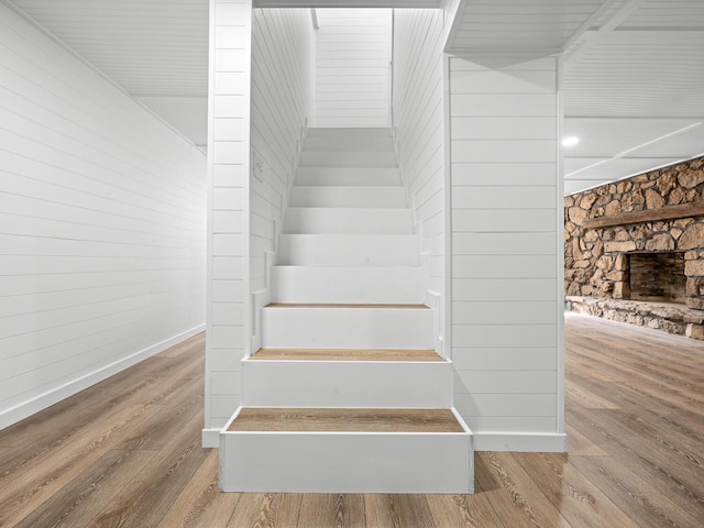 stairway with hardwood / wood-style flooring and a stone fireplace