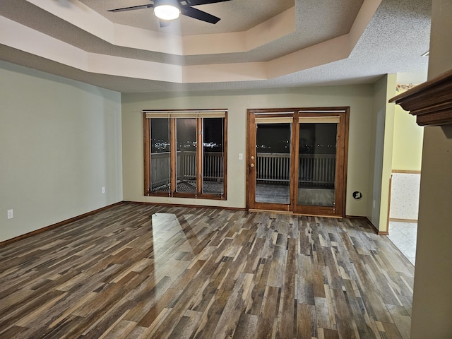 unfurnished room featuring dark hardwood / wood-style flooring, ceiling fan, a raised ceiling, and a textured ceiling