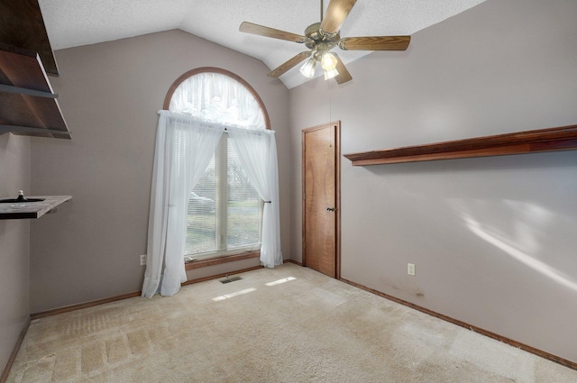 spare room with light carpet, a textured ceiling, vaulted ceiling, and ceiling fan