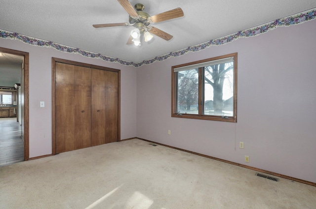 unfurnished bedroom featuring light carpet, a textured ceiling, a closet, and ceiling fan