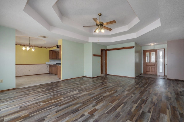 unfurnished living room featuring a tray ceiling, a textured ceiling, ceiling fan with notable chandelier, and dark hardwood / wood-style floors