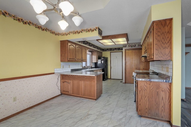 kitchen with kitchen peninsula, black fridge, stainless steel range with electric stovetop, and decorative backsplash