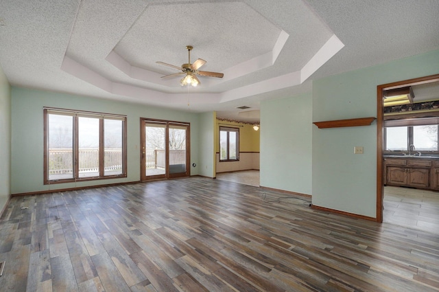 unfurnished room with ceiling fan, sink, a textured ceiling, a tray ceiling, and hardwood / wood-style flooring