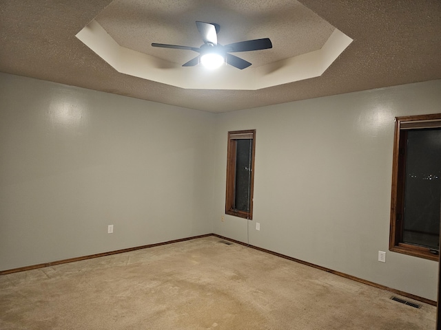 carpeted spare room featuring a raised ceiling, ceiling fan, and a textured ceiling