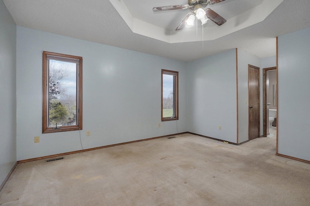 carpeted spare room with a tray ceiling and ceiling fan