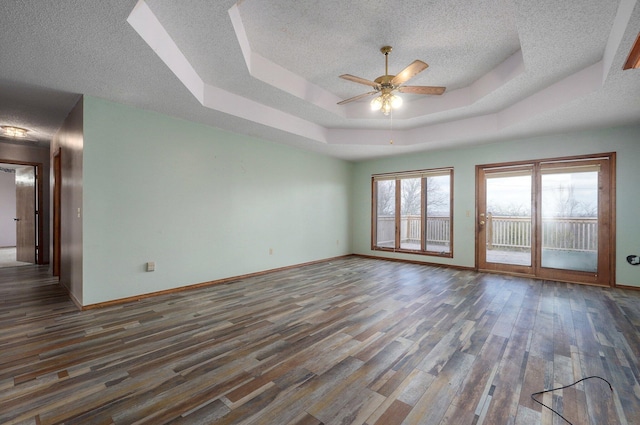 spare room featuring a tray ceiling, ceiling fan, dark wood-type flooring, and a textured ceiling