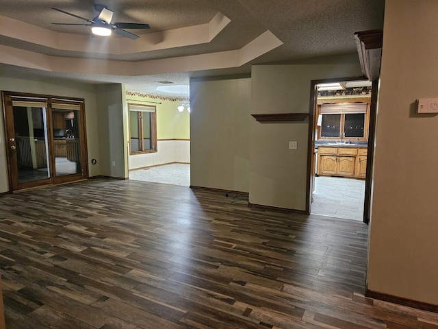 empty room with sink, ceiling fan, a textured ceiling, a tray ceiling, and dark hardwood / wood-style flooring