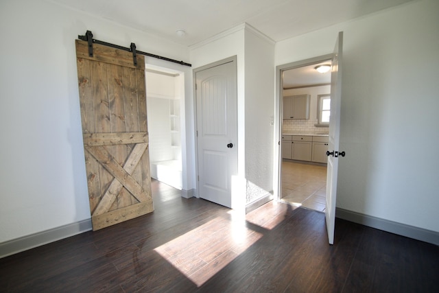 unfurnished bedroom with ensuite bathroom, a barn door, ornamental molding, and dark wood-type flooring