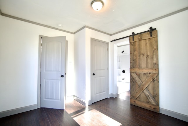 empty room with a barn door, dark hardwood / wood-style flooring, and ornamental molding