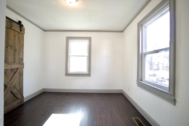 unfurnished room featuring a barn door, crown molding, dark wood-type flooring, and a healthy amount of sunlight