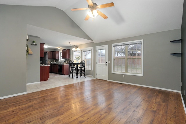 unfurnished living room featuring light hardwood / wood-style flooring, ceiling fan with notable chandelier, and vaulted ceiling