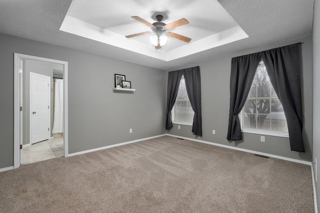 spare room with ceiling fan, light colored carpet, a textured ceiling, and a tray ceiling