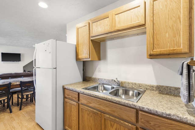 kitchen with a textured ceiling, white refrigerator, light hardwood / wood-style floors, and sink