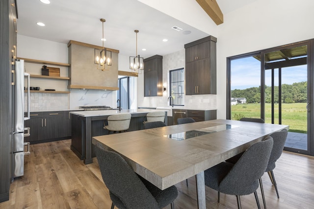 kitchen with dark brown cabinetry, a center island, beamed ceiling, light hardwood / wood-style floors, and decorative backsplash