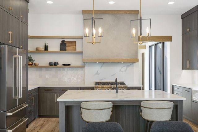 kitchen featuring light stone counters, an island with sink, pendant lighting, light hardwood / wood-style floors, and high end fridge