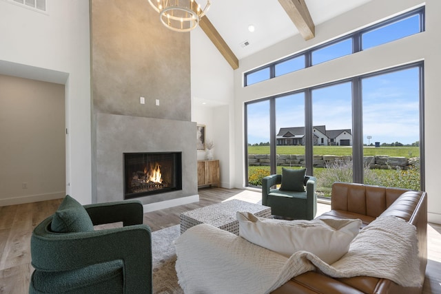 living room featuring beam ceiling, a chandelier, a towering ceiling, and light hardwood / wood-style floors