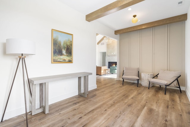 sitting room featuring beam ceiling, light wood-type flooring, and a premium fireplace