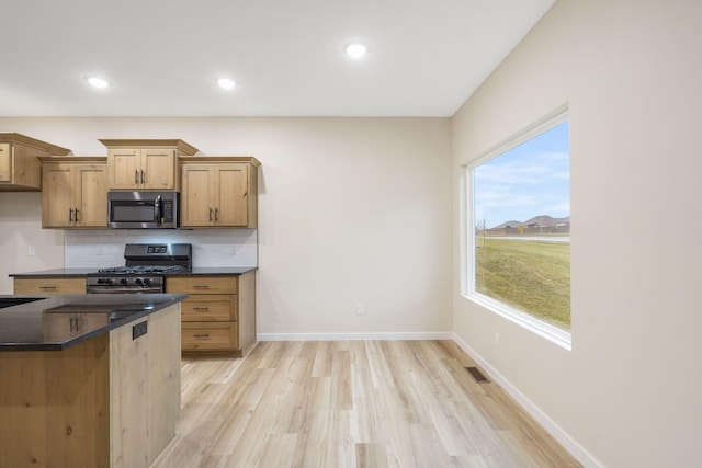 kitchen with sink, dark stone countertops, light wood-type flooring, appliances with stainless steel finishes, and tasteful backsplash