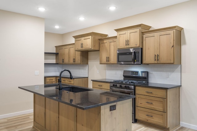 kitchen with black gas stove, light wood-type flooring, sink, and an island with sink