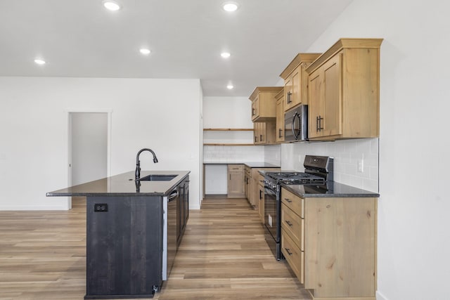 kitchen with an island with sink, sink, stainless steel dishwasher, black gas stove, and light hardwood / wood-style flooring