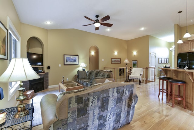 living room featuring ceiling fan, lofted ceiling, a fireplace, and light hardwood / wood-style flooring