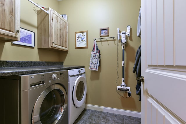 laundry area featuring washing machine and clothes dryer, dark tile patterned floors, and cabinets