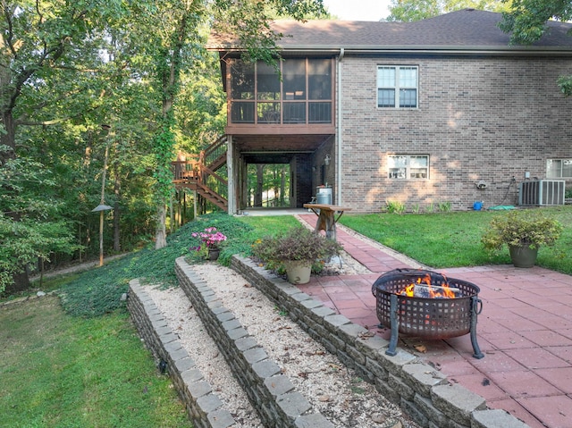 rear view of house with a sunroom, a yard, a fire pit, central air condition unit, and a patio area